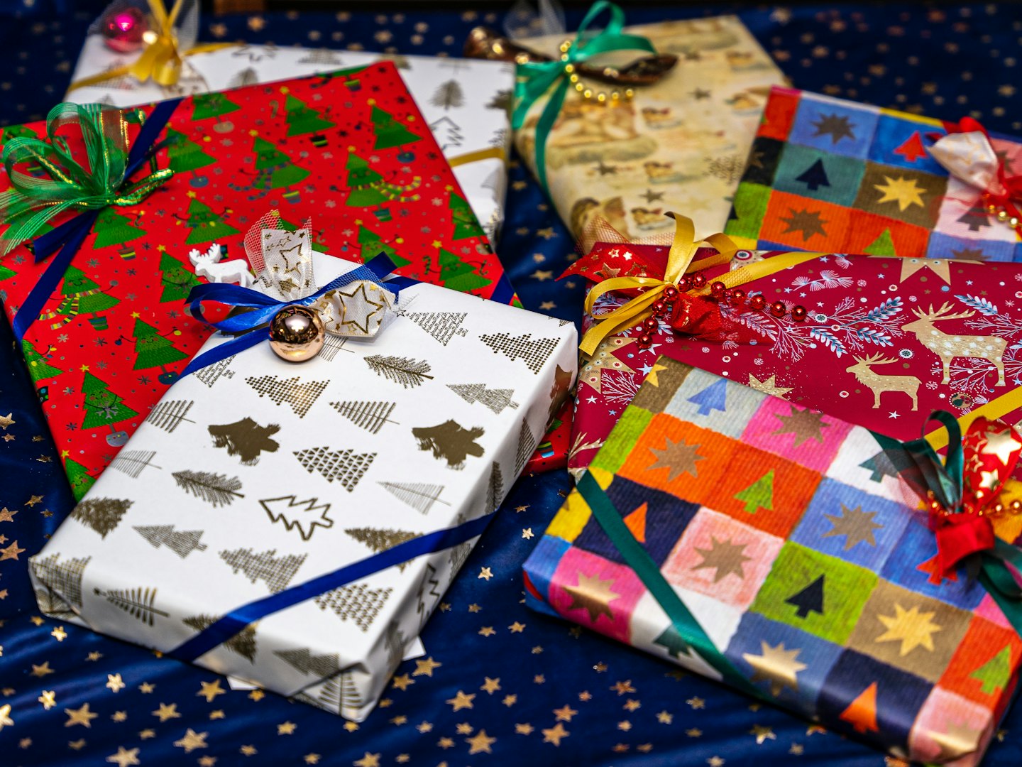 Verpackte Weihnachtsgeschenke mit Bändern und Ornamenten auf sternenklarem Stoff.