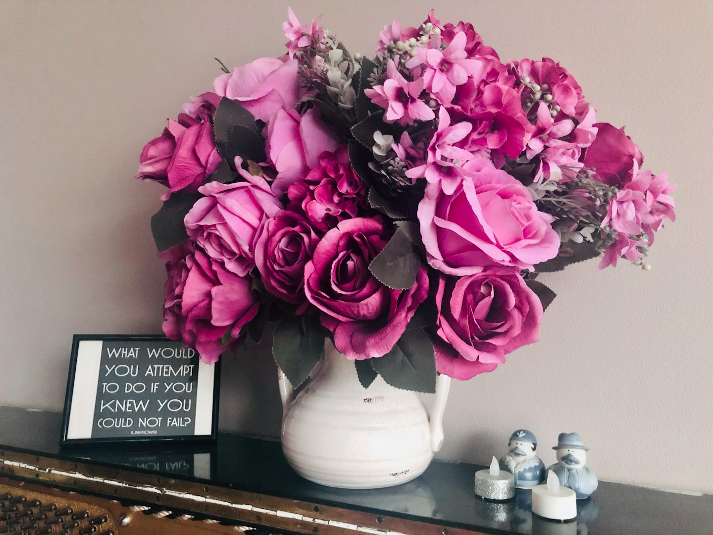 Künstliche rosa und lila Blumen in einer weißen Vase auf Holzoberfläche.