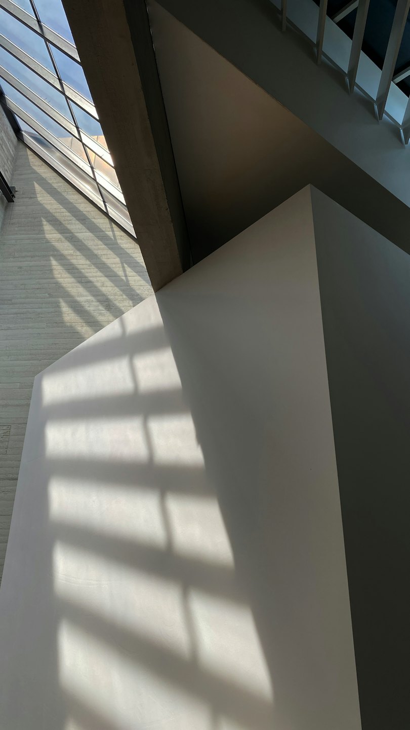 Sonnenlicht wirft geometrische Schatten auf eine graue Betonwand.